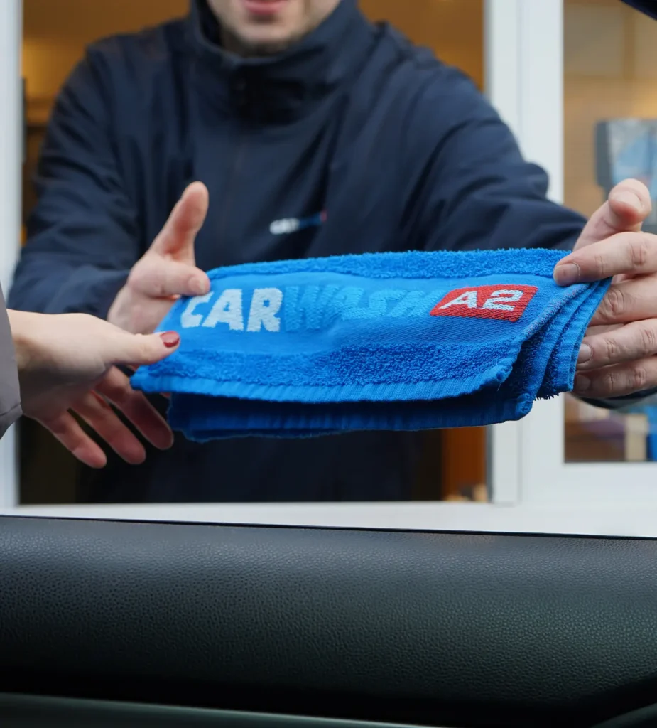 Een persoon reikt een blauwe handdoek met het opschrift "Carwash A2" aan een andere persoon.