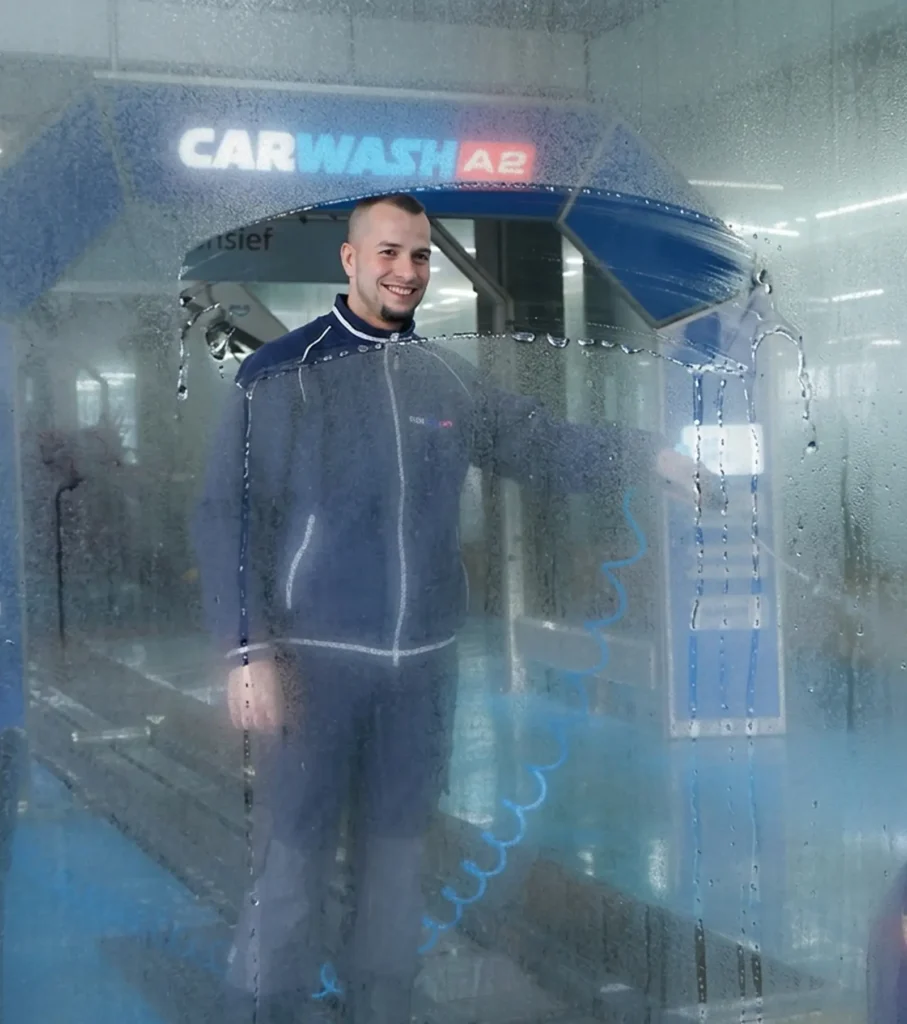 Een man in een blauwe overall staat achter beslagen glas bij een carwash.