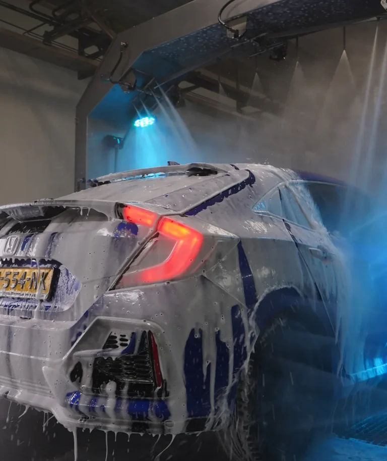 Een auto wordt gewassen in een automatische wasstraat met sop en waterstralen.