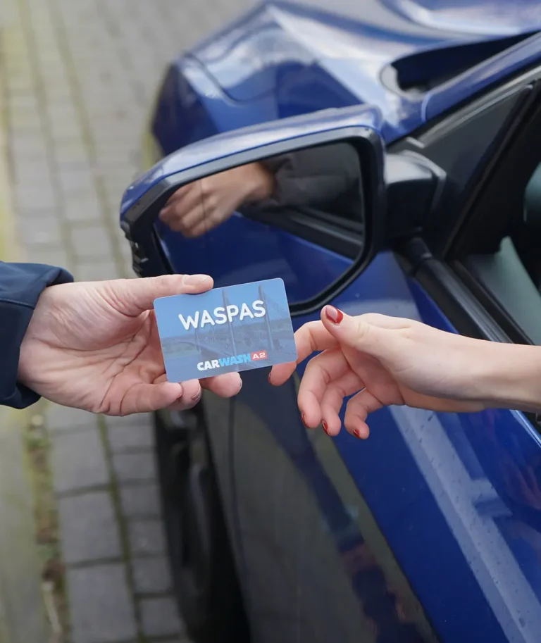 Twee personen wisselen een Waspas uit bij een blauwe auto.