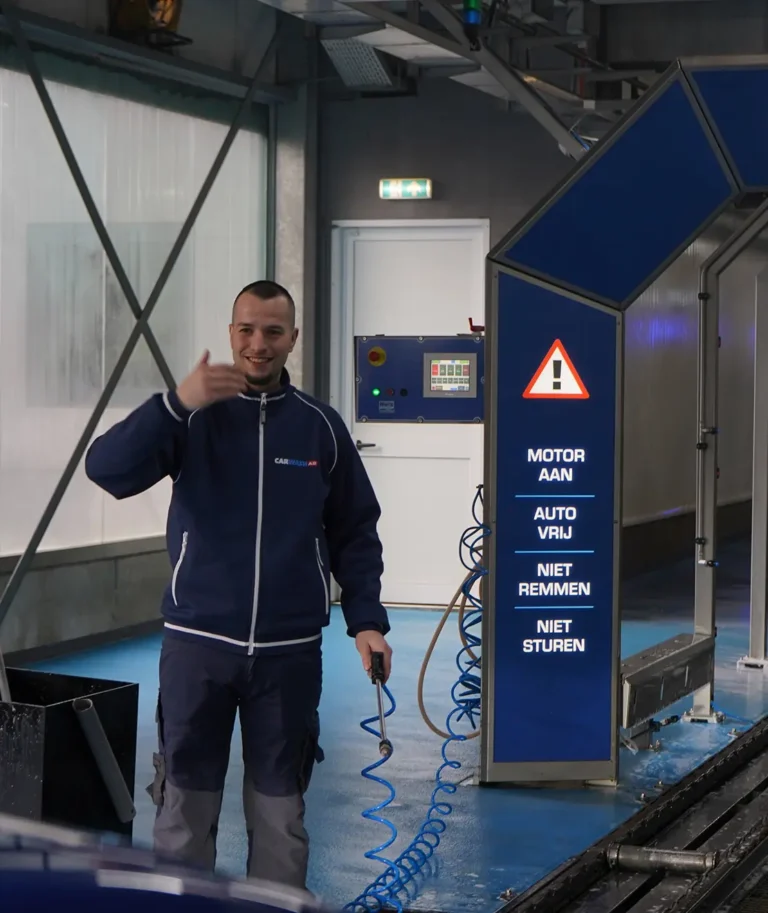 Een medewerker van een autowasstraat geeft een duim omhoog naast een bord met instructies voor de wasstraat.