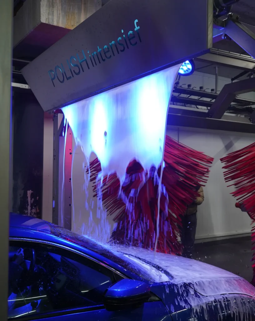 Auto wordt gewassen bij een milieuvriendelijke en duurzame wasstraat onder blauw licht met schuim en borstels.