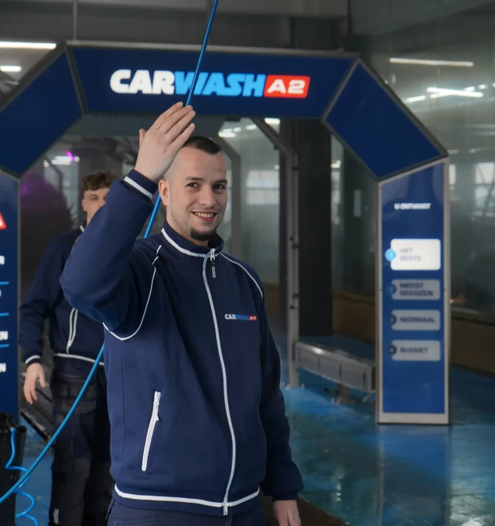 Een medewerker van Carwash A2 zwaait met een glimlach in de wasstraat.
