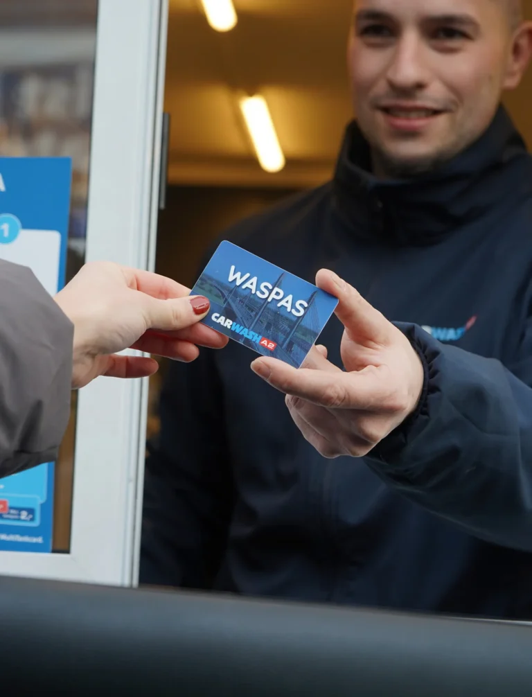 Een medewerker overhandigt een Waspas aan een klant bij een carwashbalie.